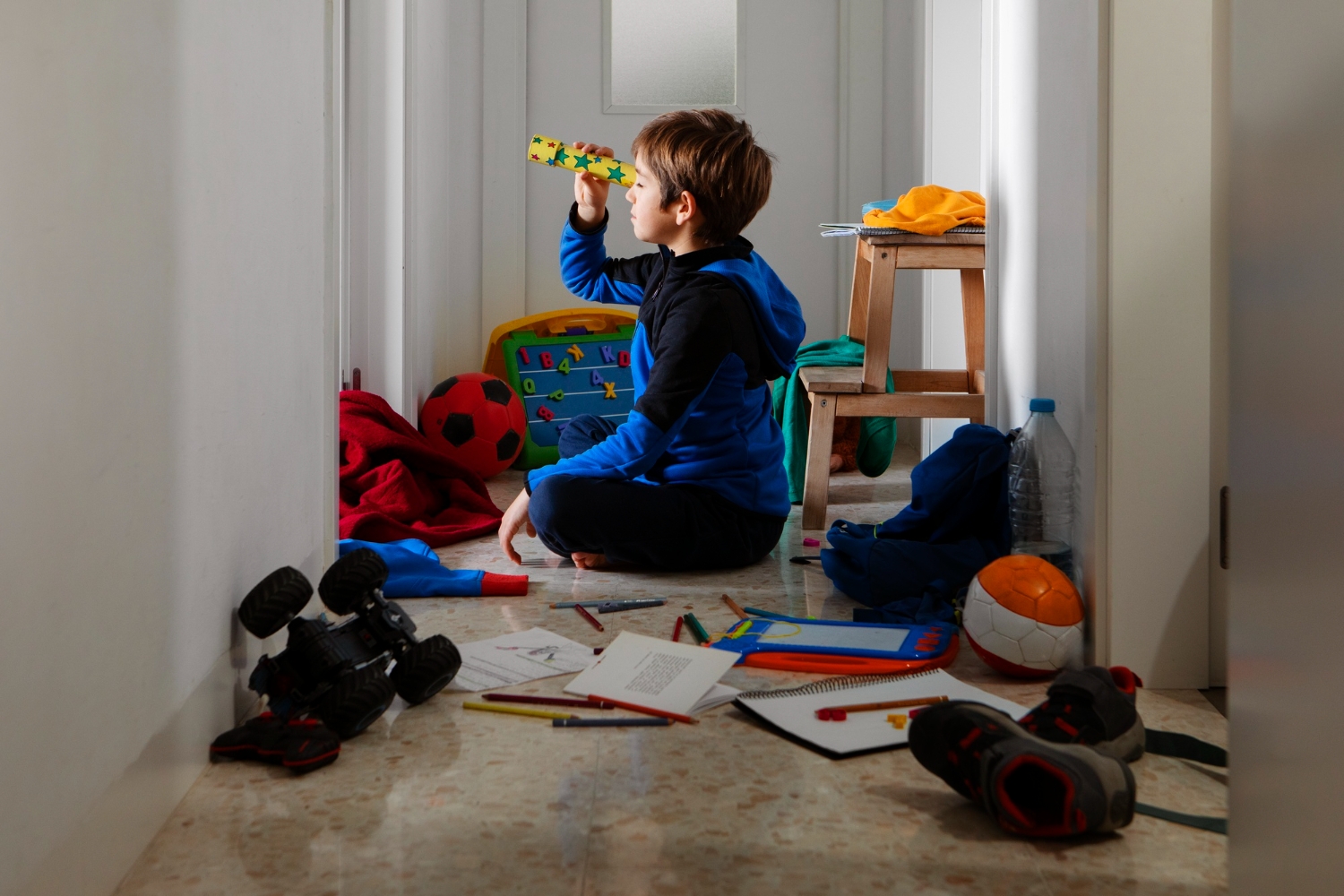 Child in chaotic hallway, playing with a kaleidoscope toy